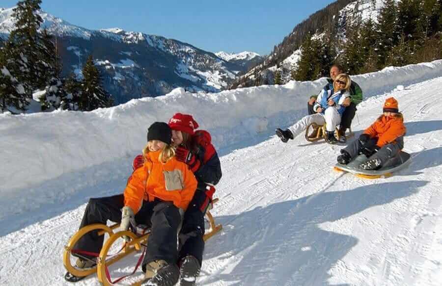 Familien beim Schlittenfahren auf schneebedecktem Hügel in den Alpen.