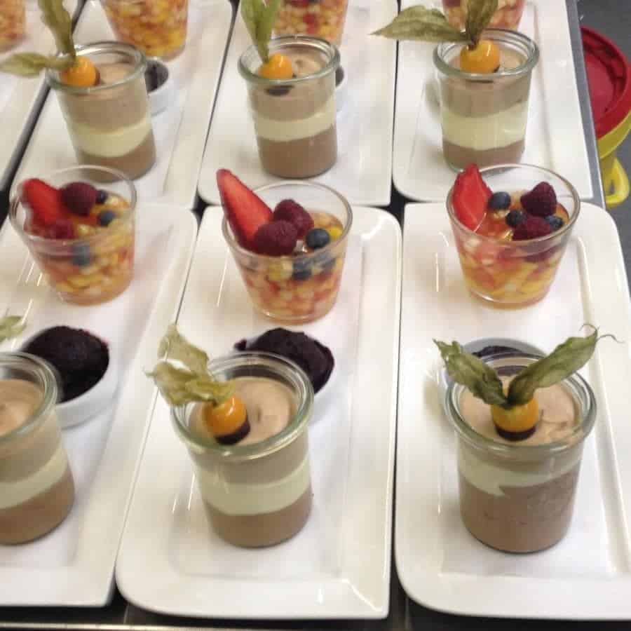 Desserts in Gläsern: bunte Früchte, Creme-Schichten und Dekoration aus Beeren und Blättern.