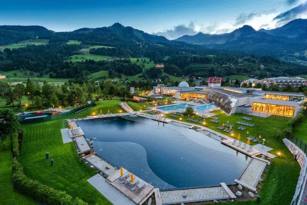 View of Hotel Steindlwirt with swimming pond and mountain landscape in the background.