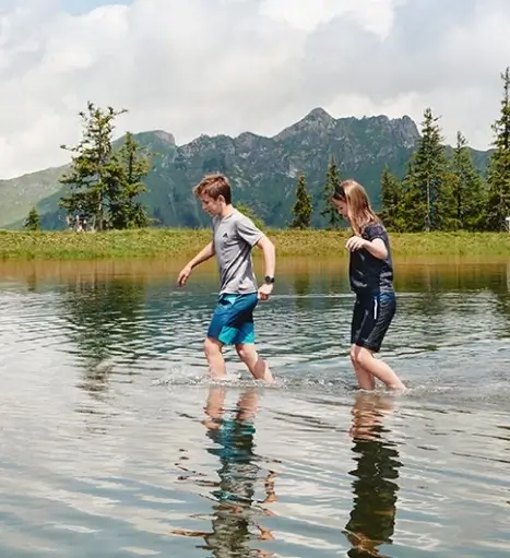 Two children wading through a refreshing mountain lake in the Gastein active region.