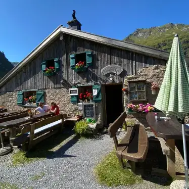 Gemütliches Berghaus mit Terrasse, umgeben von Blumen und Bergen, ideal für eine Auszeit.