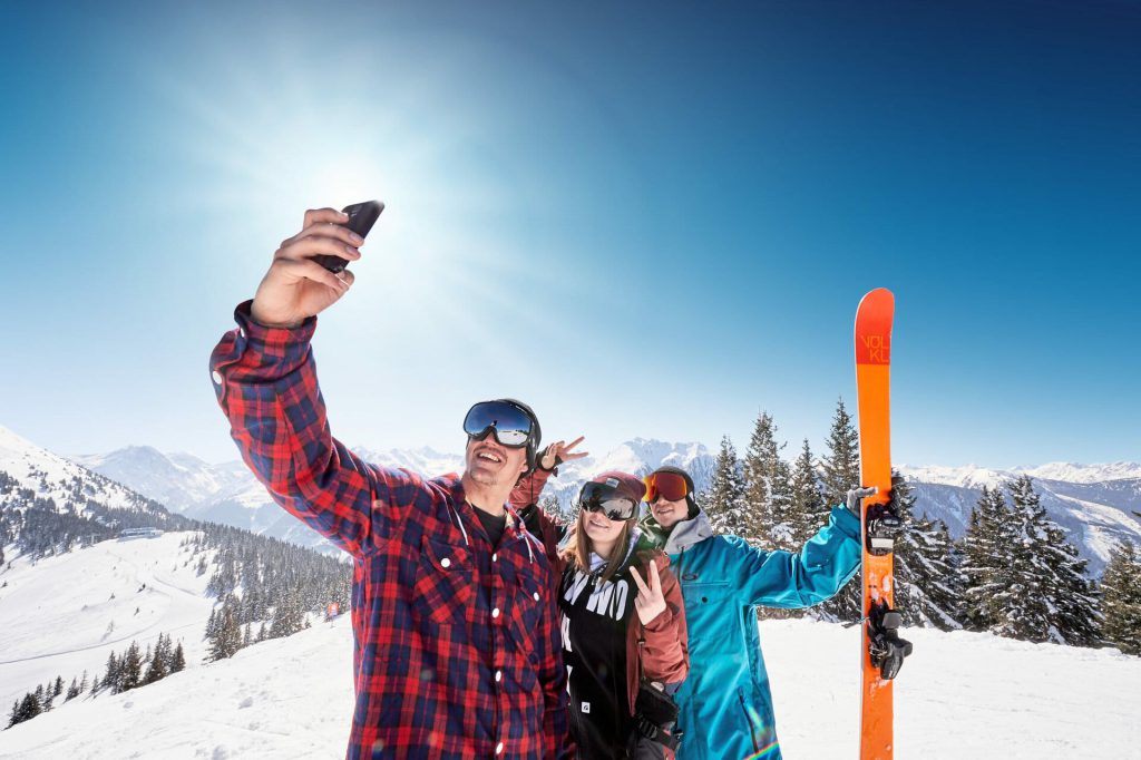 Skiende Freunde machen ein Selfie in den Bergen bei strahlendem Sonnenschein.