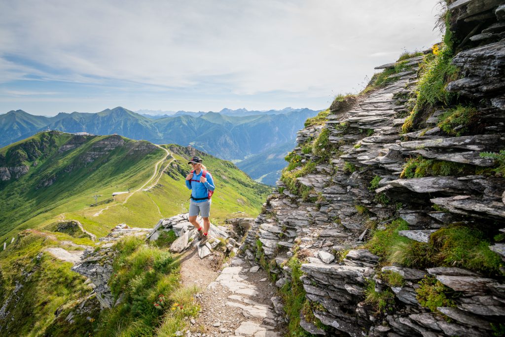 Wanderer auf schmalem Bergpfad mit Aussicht auf grüne Alpen im Gasteinertal