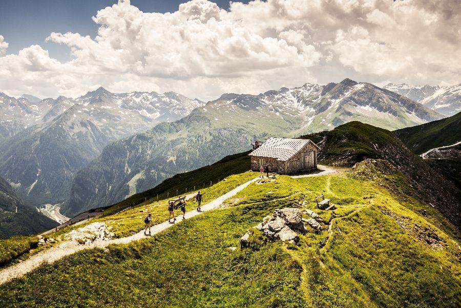 Wandelaars op bergpad met hut en Alpenpanorama