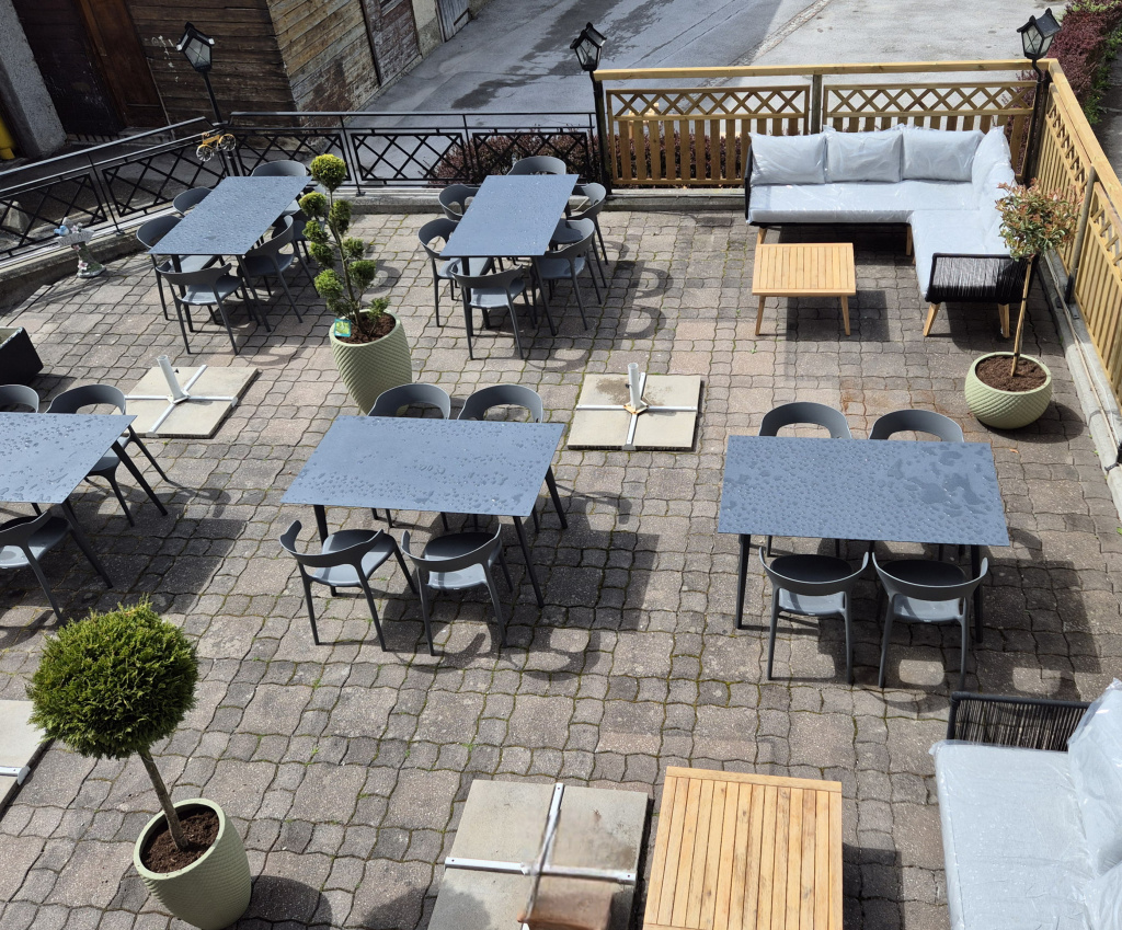 Nasse Außenterrasse mit grauen Tischen, Stühlen und Sitzlounge