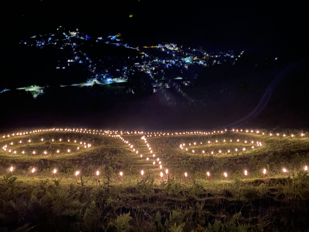 Bergfeuer leuchten nachts am Hang über einem beleuchteten Ort im Tal