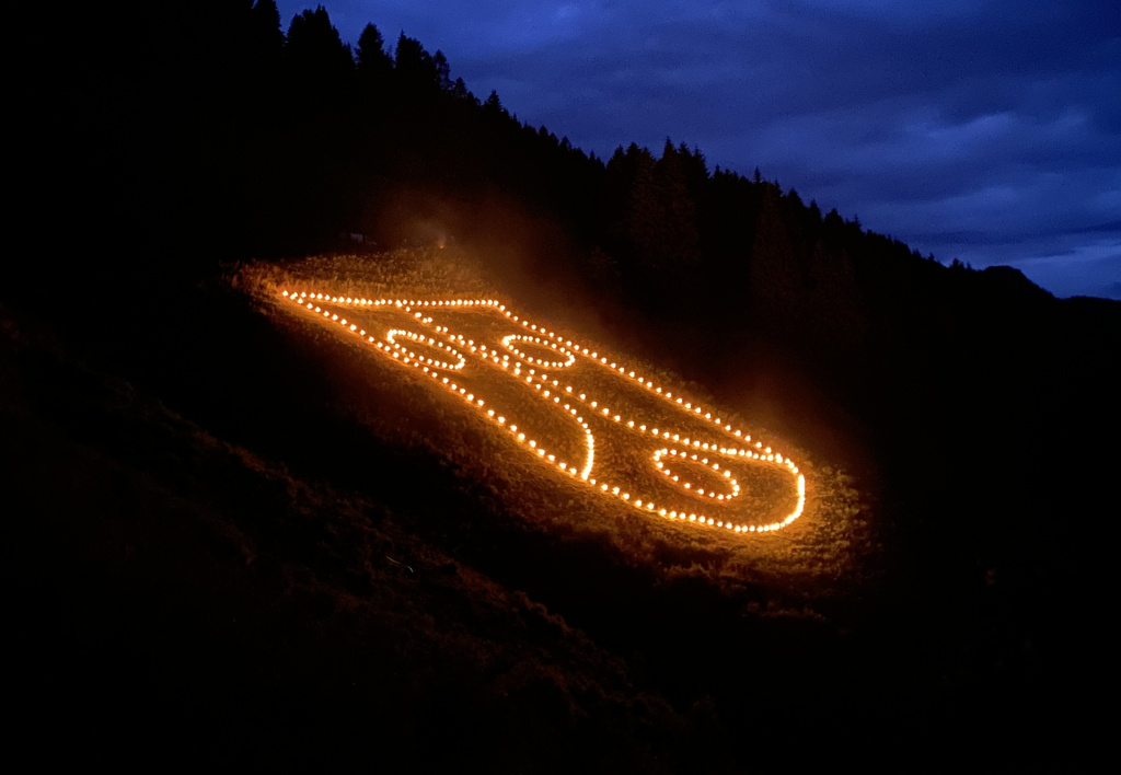Bergfeuer zeichnen leuchtende Linien an einen dunklen Berghang unter blauem Abendhimmel