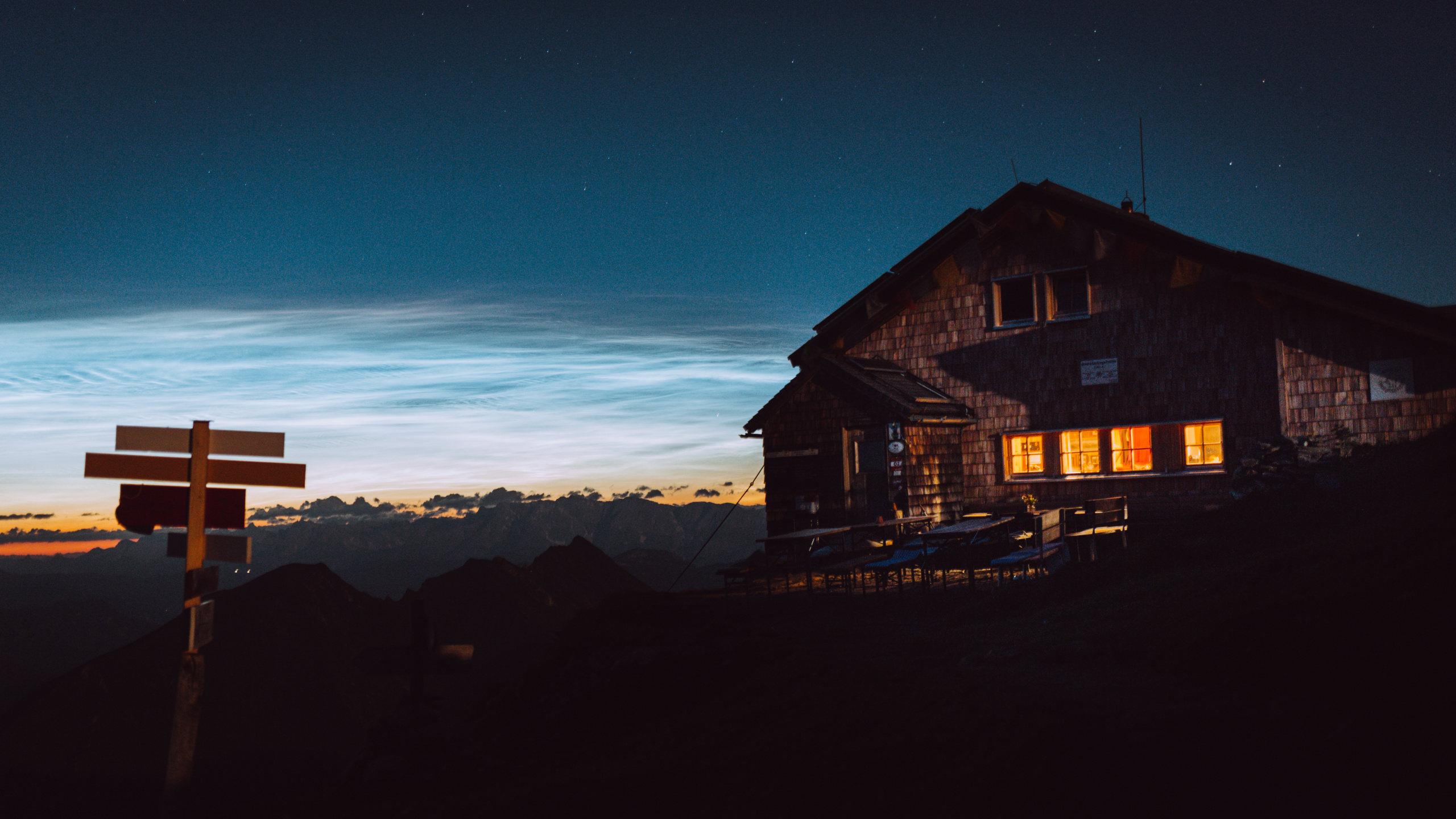 Sternenhimmel über alpinen Holzhütten mit hellen Lichtspuren in der Dämmerung