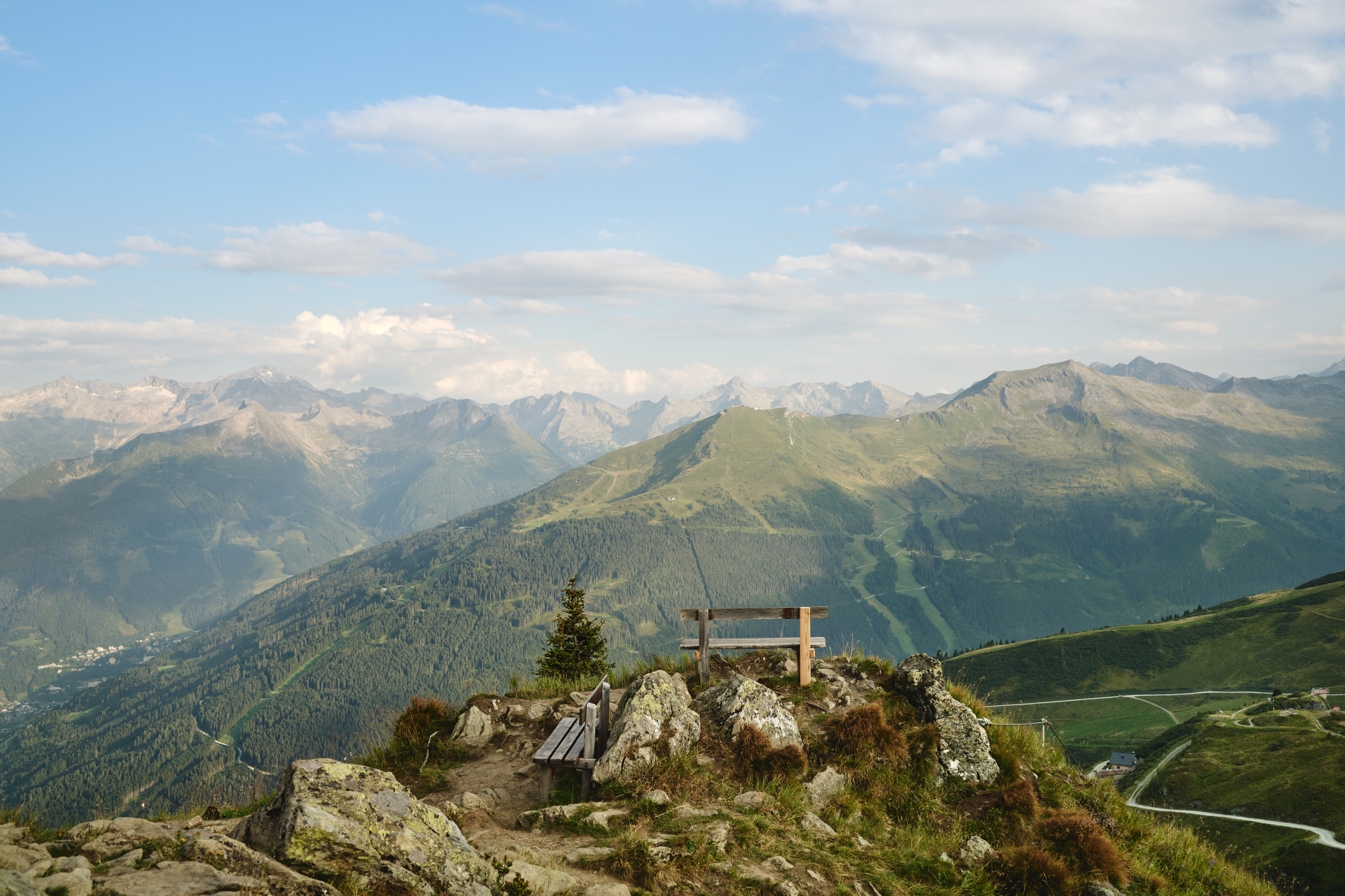 Holzbänke auf felsigem Berggrat mit weitem Blick über grüne Alpenhänge und Gipfel